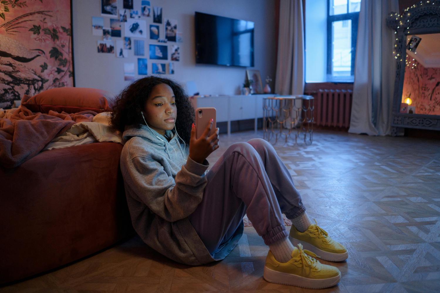teen girl leaning on bed with earphones in looking at phone